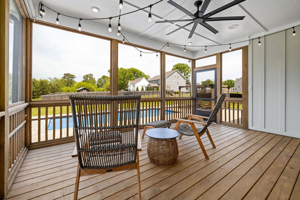 Wood deck on a screened porch with armchairs and a pool in the background