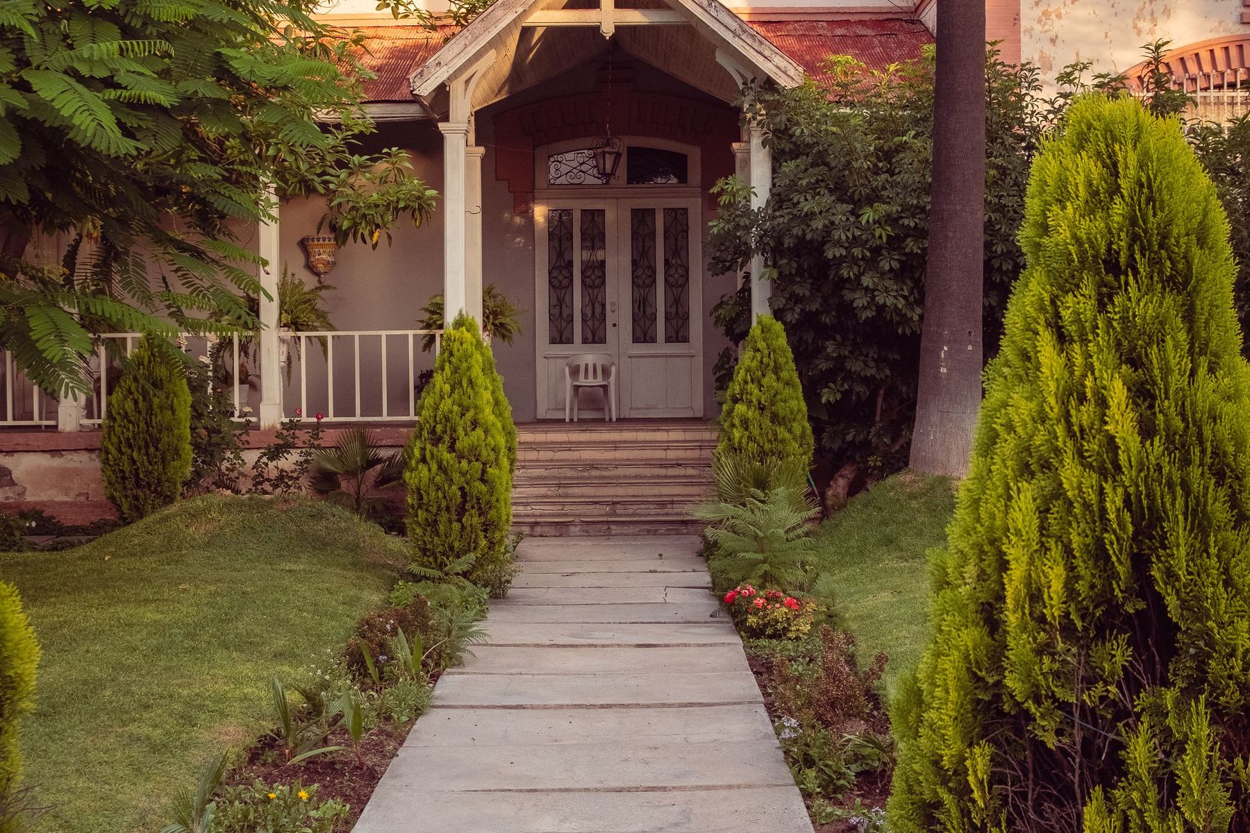 Stone walkway through a garden leading to a house with a covered porch
